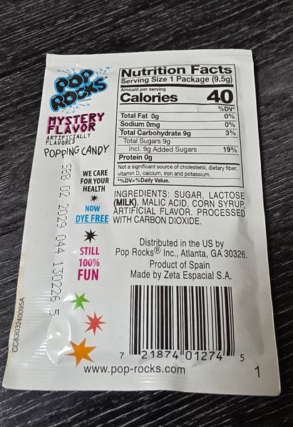 A close-up of the back of a Pop Rocks Mystery Flavor Popping Candy package, showing nutrition facts, ingredients, and a barcode, placed on a dark wood surface.