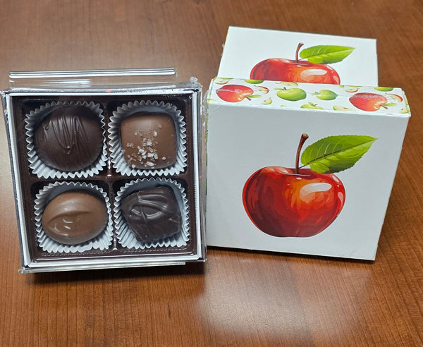 Box of chocolates with a decorative lid featuring apple illustrations on a wooden surface.